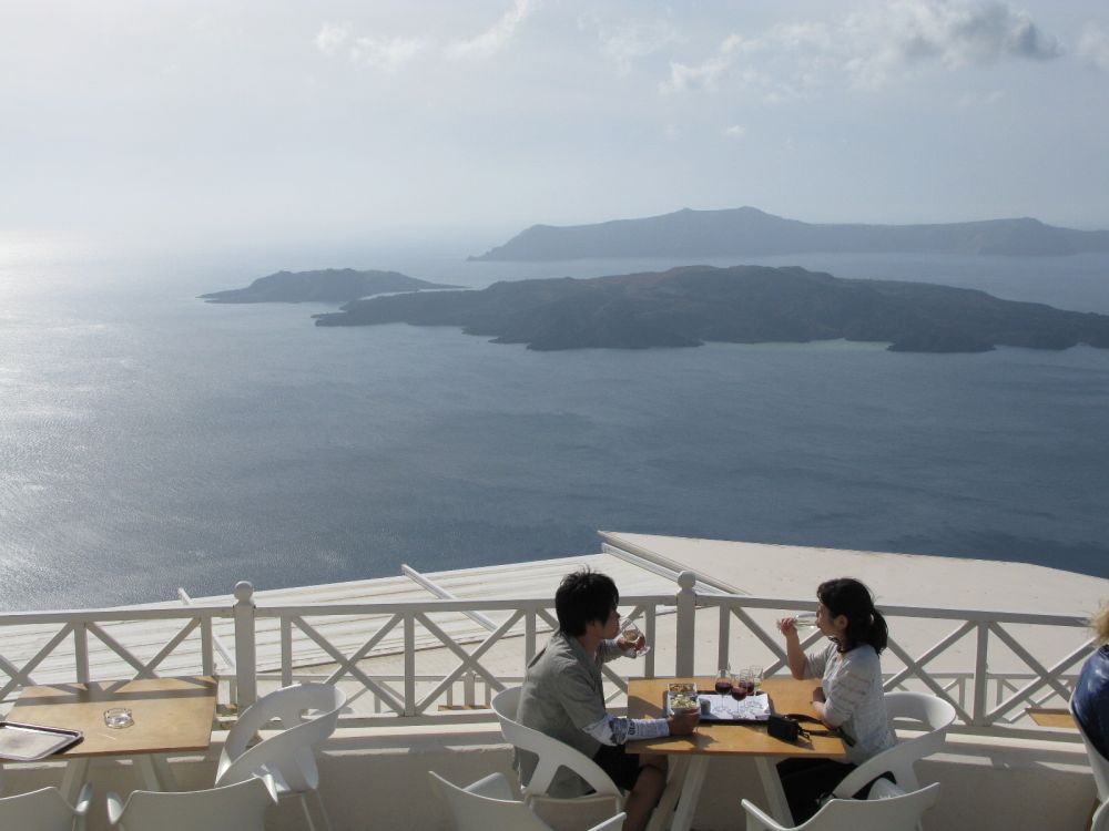 An Asian couple, holidaying on Santorini, enjoys the view while sampling the island's variety of wine.