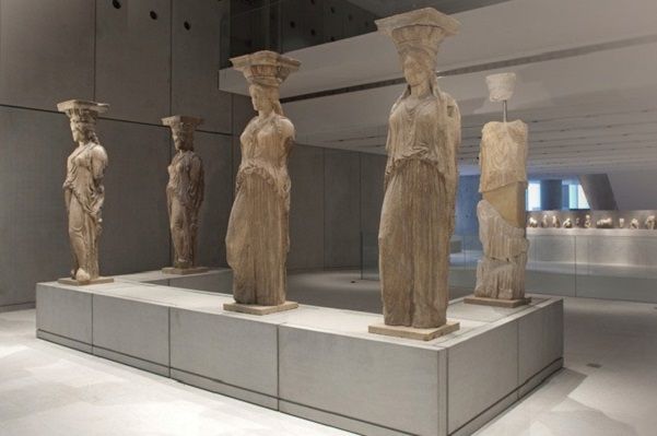 The renowned Caryatids in the Acropolis Museum. The figures were originally six but one was removed by Lord Elgin in the early 19th century and is now in the British Museum in London. The pedestal for the Caryatid removed to London (second from the left on the front) remains empty. Photo Source: Acropolis Museum