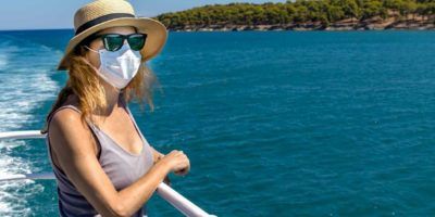 Woman standing outdoors on ferry ship with a surgical mask during Covid-19 travelling in Greece. Photo source: Shutterstock